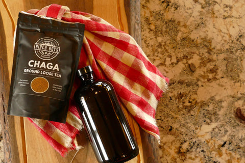 Black chaga ground loose tea package and amber glass bottle on a wooden surface with a red and white checkered cloth.