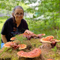 Woman sits with red reishi mushrooms