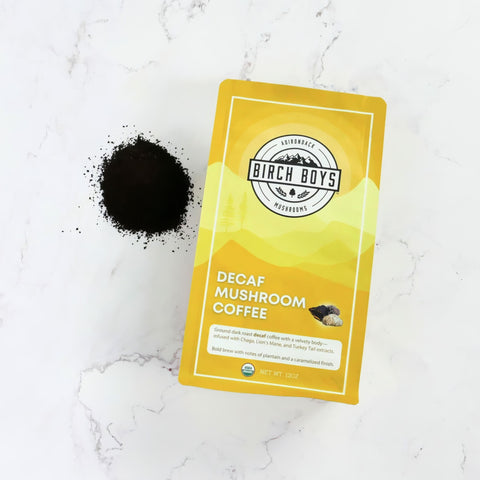Decaf Mushroom Coffee box on a white granite surface with a small pile of ground coffee next to it