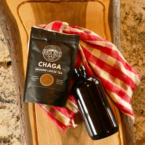 Birch Boys Chaga Ground Loose Tea package with a black bottle on a wooden surface with a red and yellow checkered cloth.
