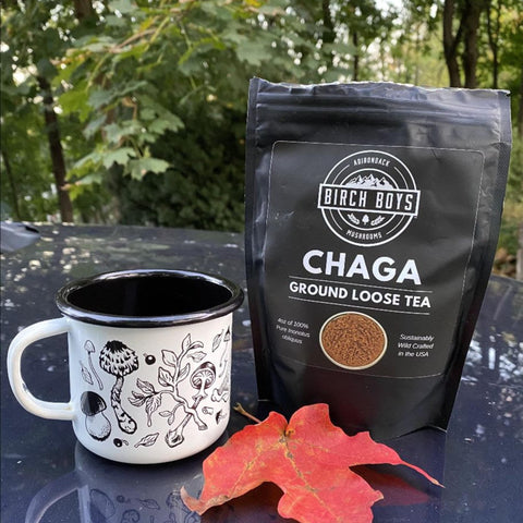 Birch Boys Chaga ground loose tea package with a mug on a reflective surface outdoors.