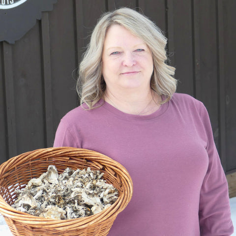 Woman holding a basket of maitake mushrooms against a wooden background