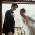 Man and woman in wedding attire standing close together, smiling.